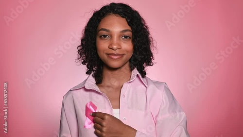 Breast cancer awareness concept.Smiling,cheerful girl with pink ribbon on pink background.October