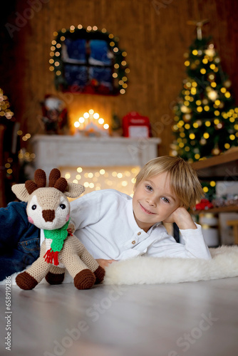 Beautiful blond child, young school boy, playing in a decorated home with knitted toys
