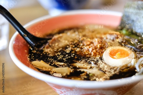 A bowl of tonkotsu ramen with black garlic sauce, chargrilled chashu pieces, bamboo shoots, soft-boiled egg and ladle spoon at Mikazuki, a Japanese restaurant in Sydney photo