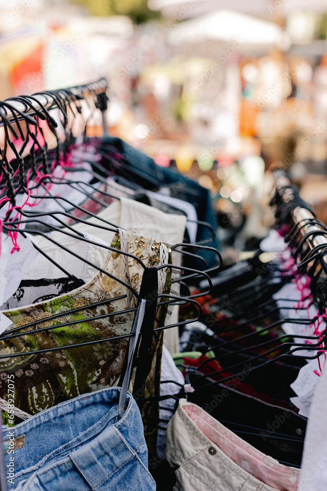 Naklejka premium Choice of fashion clothes of different colors on hangers in a retail shop. Flea market with old clothes outside. Reduce Reuse Recycle concept