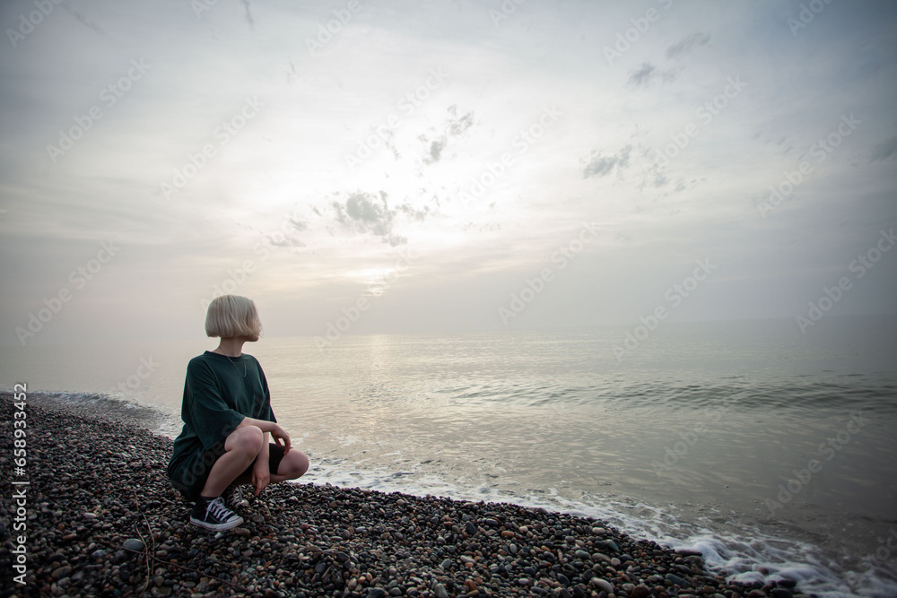 Beautiful young blonde woman sitting on sea beach