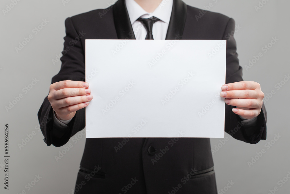 White empty blank paper board banner in hand of businessman in formal suit on grey background White empty blank paper board banner in hand of businessman in formal suit on grey background