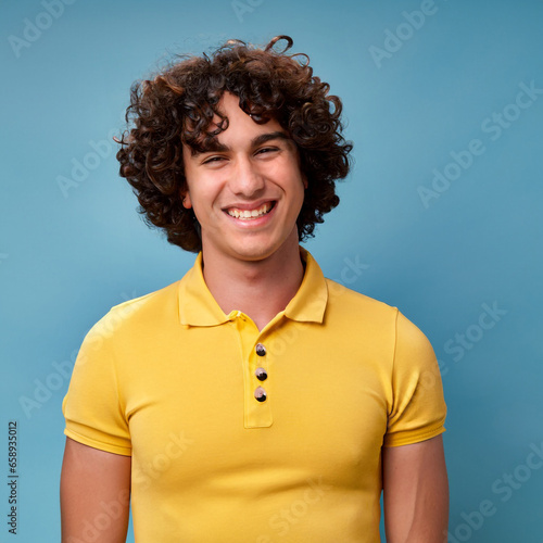 Funny curly hair man smiling and laughing, wearing a yellow t shirt on a bright solid blue background. created by generative AI technology