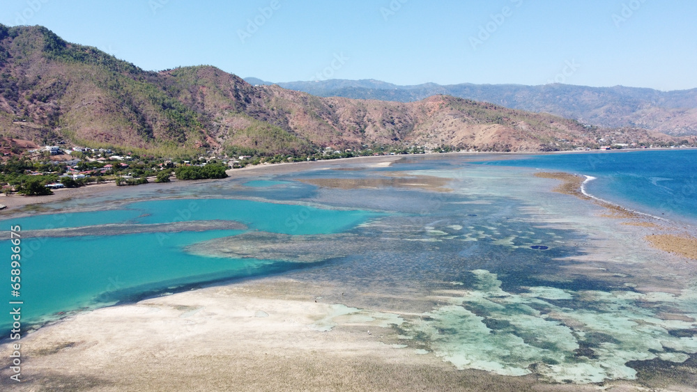 Scenic view of rugged hills, coastal road and beautiful ocean with crystal clear turquoise water, coral reefs and patterned sand in Dili, Timor-Leste, Southeast Asia