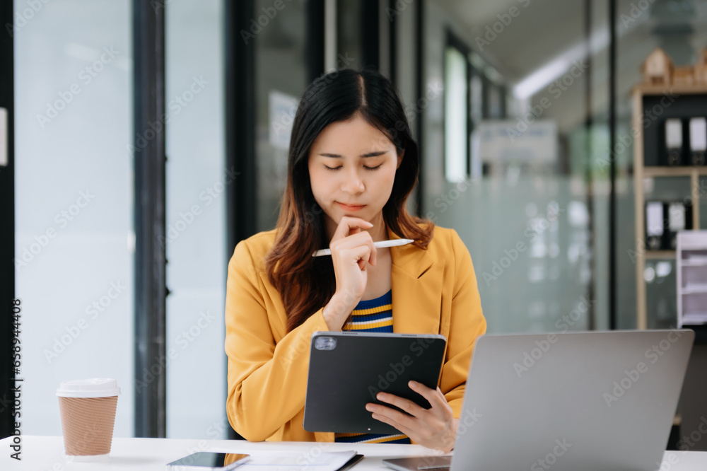 Confident business expert attractive smiling young woman typing laptop ang holding digital tablet on desk in office. Confident business expert attractive smiling young woman typing laptop ang holding digital tablet on desk in office.