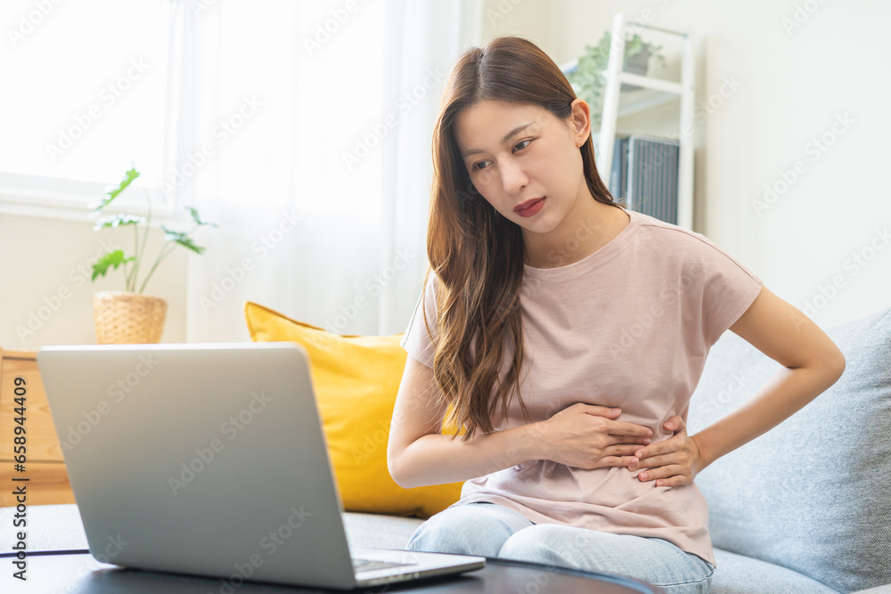 Telehealth, Telemedicine concept. Flatulence asian patient young woman stomach ache suffer from food, discussing with doctor video call with computer at home, during online consultation in living room Telehealth, Telemedicine concept. Flatulence asian patient young woman stomach ache suffer from food, discussing with doctor video call with computer at home, during online consultation in living room