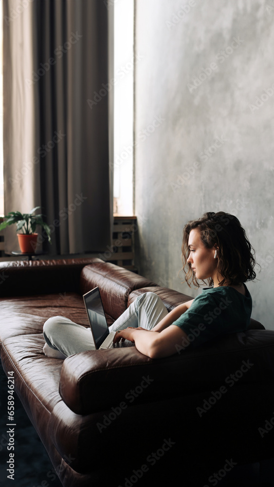 Naklejka premium Productive Home Workspace: Young Woman Working on Laptop, Illustrating the Concept of Work or Study from Home, Freelancing, Business, and Modern Lifestyle for Students and Professionals