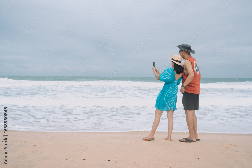Asian tourist couple taking selfies, sand on beach and blue summer sky with white waves, summer vacation and holiday concept. Asian tourist couple taking selfies, sand on beach and blue summer sky with white waves, summer vacation and holiday concept.