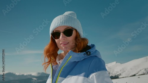 Low angle shot of female tourist on winter vacation. Winter equiped woman in the mountains having eye contact with camera. photo