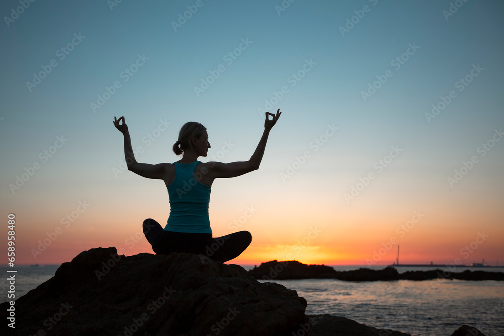Silhouette of a yoga woman sitting on the seashore at sunset.