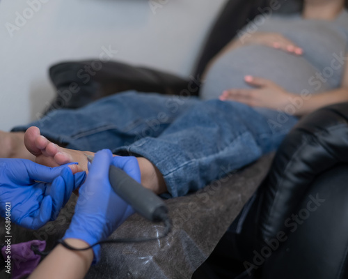Pregnant woman on a hardware pedicure procedure in a beauty salon. 