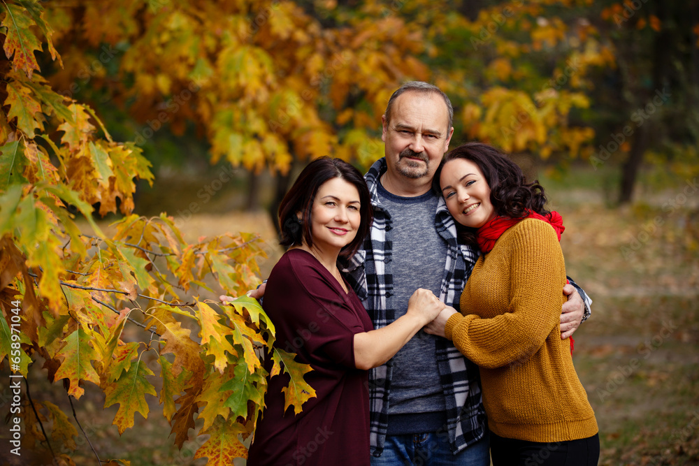 Fototapeta premium autumn portrait of middle-aged parents and their adult daughter on a walk outdoors. Family of respectable age in autumn park. Happy family story. Together during all their life. Warm autumn sunny days