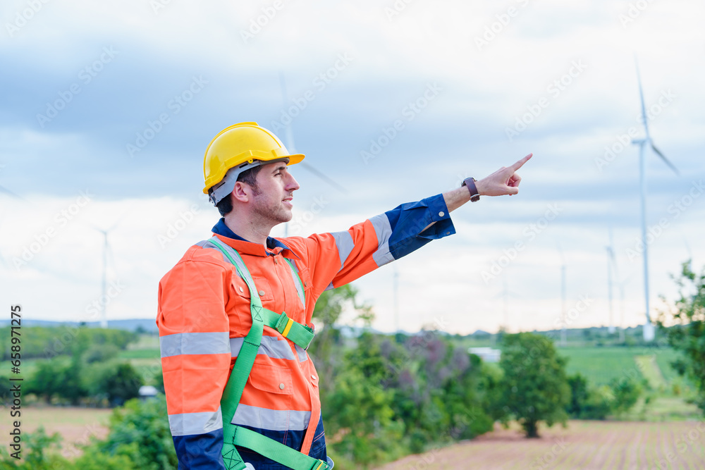 Maintenance engineer team worker building looking for wind turbines blueprint drawings and point finger on windmill field farm Alternative renewable energy for clean energy concept.