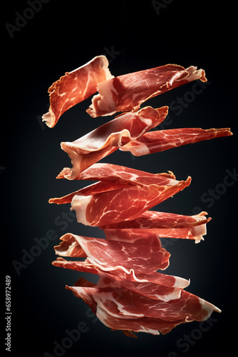 Thin slices of Spanish ham jamon flying in the air on black background. Traditional meat specialty of the local cuisine photo
