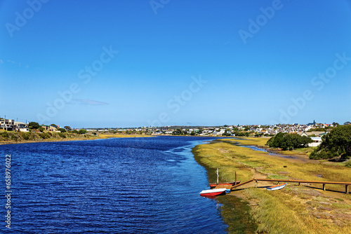 Description Broad Goukou river estuary with small jetty and boat flowing through the town of Still Bay in the Western Cape, South Africa