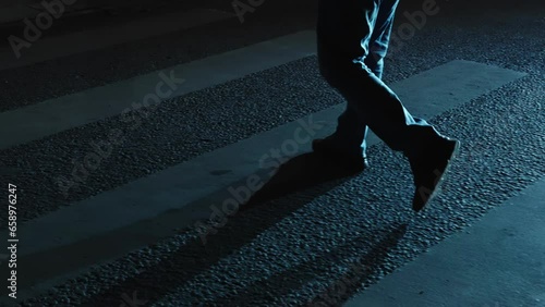 Men's feet walking on a pedestrian crossing in the night city. Slow motion, light from car headlights.