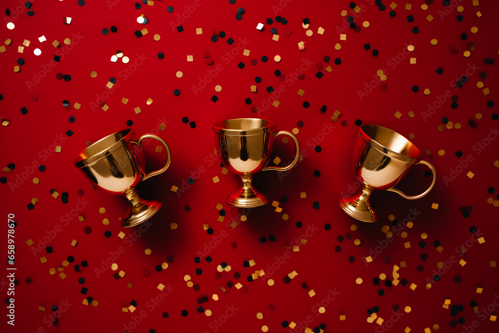 golden winners cups flat lay on a red background with golden confetti