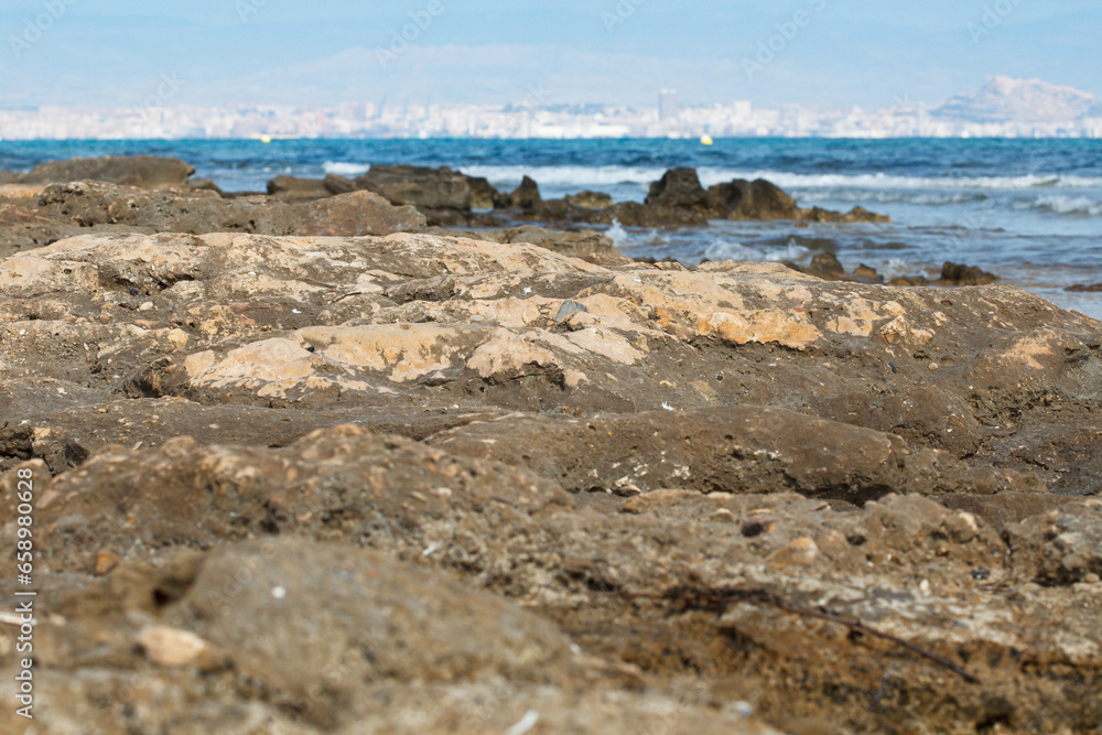 Playa de piedra en los Arenales del Sol con fondo desenfocado del mar mediterraneo y la ciudad de Alicante, España