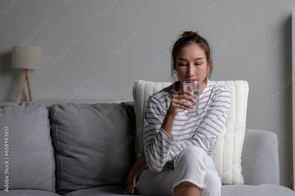 Asian woman drinking cold water while sitting on the sofa at home. Female drinking clean water health. Asian woman drinking cold water while sitting on the sofa at home. Female drinking clean water health.
