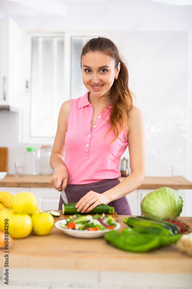 Cheerful young woman preparing vegetable salad for dinner at home