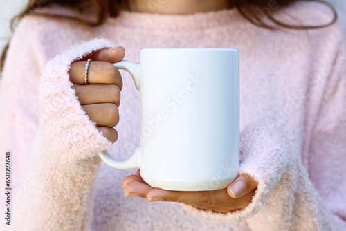 Fotografie Girl is holding blank large white porcelain mug in hands and soft pink sweater