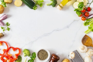 Frame of healthy food cooking ingredients background with fresh vegetables, herbs, spices and olive oil on marble table top view