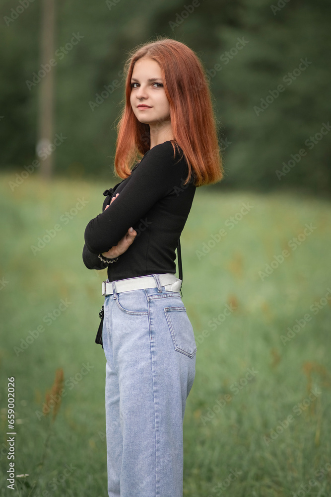 Portrait of a young beautiful red-haired girl in jeans and a black sweater outdoors. Portrait of a young beautiful red-haired girl in jeans and a black sweater outdoors.