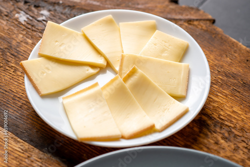Plate with slices of sliced cheese on wooden background