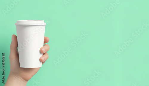 Mockup. Hand holding a recycleable cup of take away coffee on a green background, copy space on the right photo