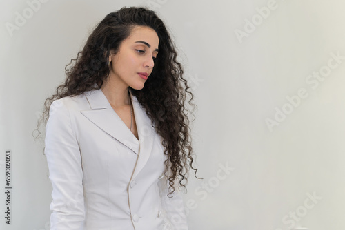 A poised young woman in a white suit casts a serious glance. As a cosmetologist, her dedication reflects in her eyes.