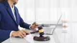 Lawyer woman holding wooden judge gavel and reading business contract with law agreement on laptop