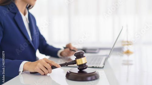 Lawyer woman holding wooden judge gavel and reading business contract with law agreement on laptop