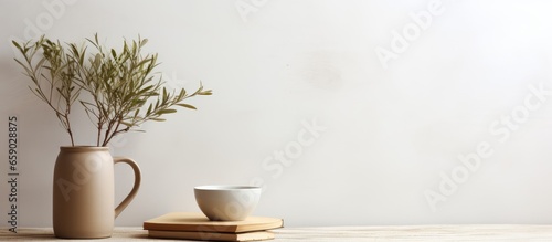 Minimalistic Scandinavian interior with an olive tree branch in a beige vase a brown cup of coffee tea and old books on a wooden table against a white wall background in the dining room crea