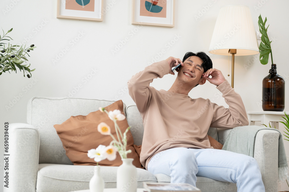 Happy asian man sitting on couch using smartphone in living room at home, relax time and lifestyle concept Happy asian man sitting on couch using smartphone in living room at home, relax time and lifestyle concept