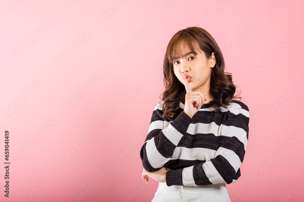Woman making finger on lips mouth silent quiet gesture, Happy Asian beautiful young female marking silence for stop quiet, mute studio shot isolated on pink background with copy space
