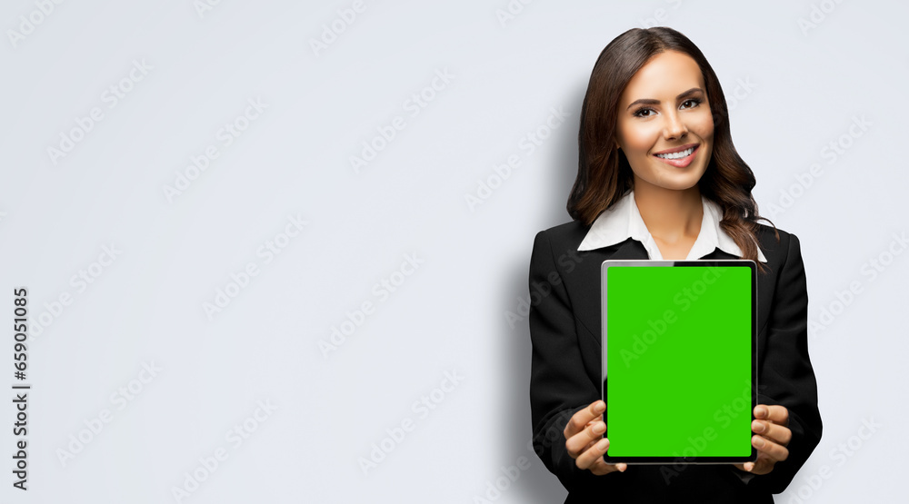 Portrait of happy smiling brunette businesswoman showing tablet pc, touchpad, with green chroma key screen, against lightly grey gray background. Confident attractive business woman at office. Portrait of happy smiling brunette businesswoman showing tablet pc, touchpad, with green chroma key screen, against lightly grey gray background. Confident attractive business woman at office.