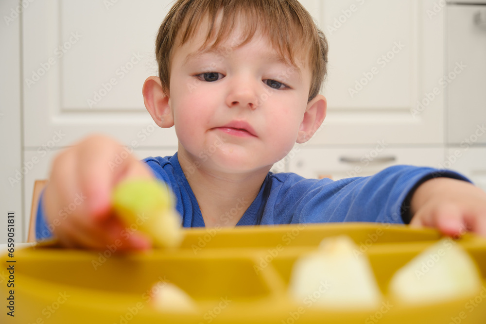 The child happily snacks on a plate full of fresh fruits and berries at home. Kid boy aged two years (two-year-old) The child happily snacks on a plate full of fresh fruits and berries at home. Kid boy aged two years (two-year-old)