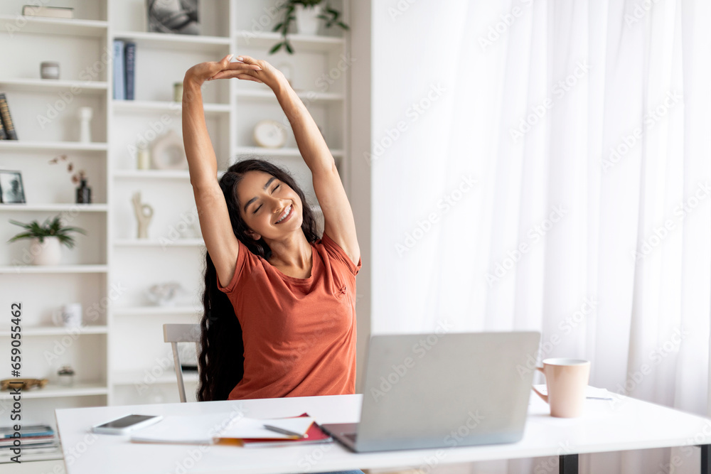Joyful young indian woman stretching body at home office