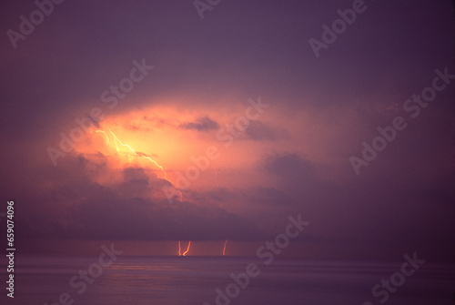 Lightning strikes over the ocean at sunset.