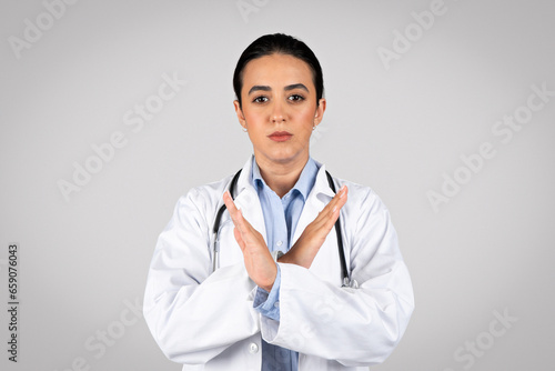 Serious woman doctor confidently showing no gesture over grey background © Prostock-studio