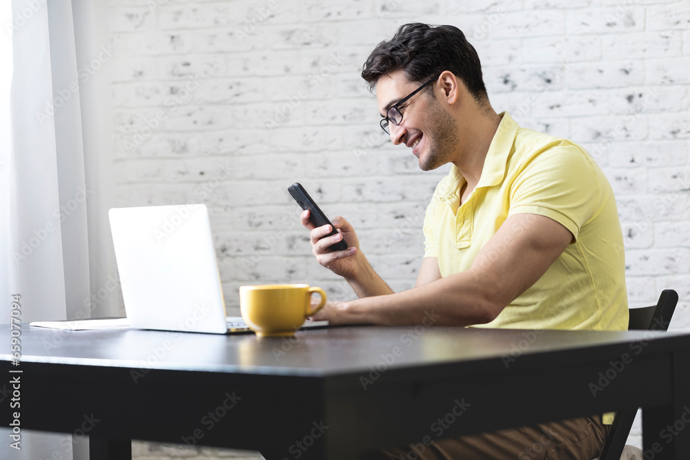 Portrait of smiling young freelancer working on laptop and looking at smartphone. Distant work concept Portrait of smiling young freelancer working on laptop and looking at smartphone. Distant work concept