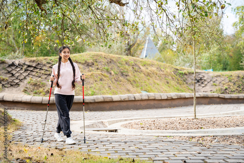 Nordic walking. Young Indian woman walking with Scandinavian sticks in the city park.