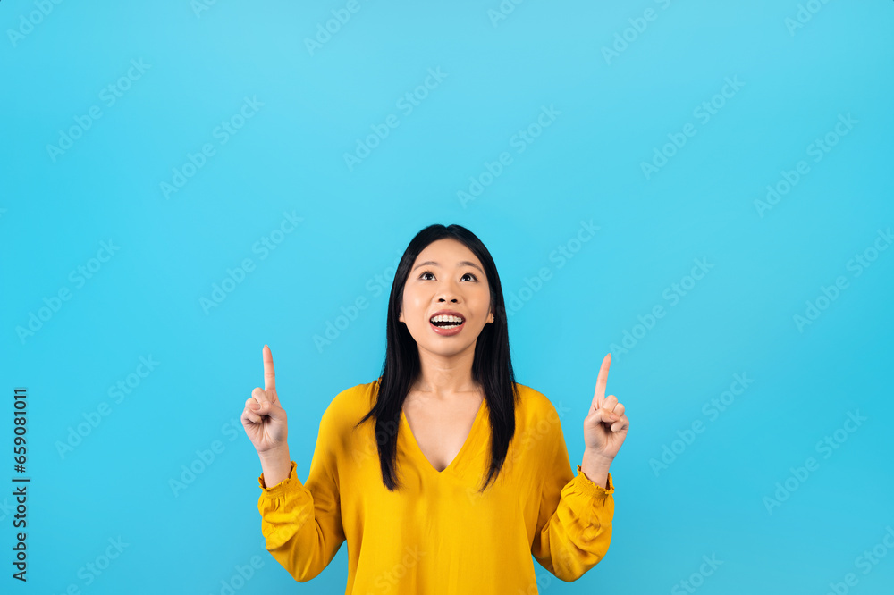 Cheerful young asian lady pointing at copy space above head Cheerful young asian lady pointing at copy space above head