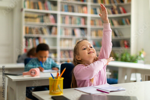 Smart schoolgirl raising hand to answer in class