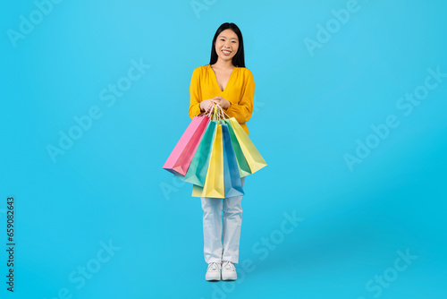 Positive young asian lady showing shopping bags, blue background