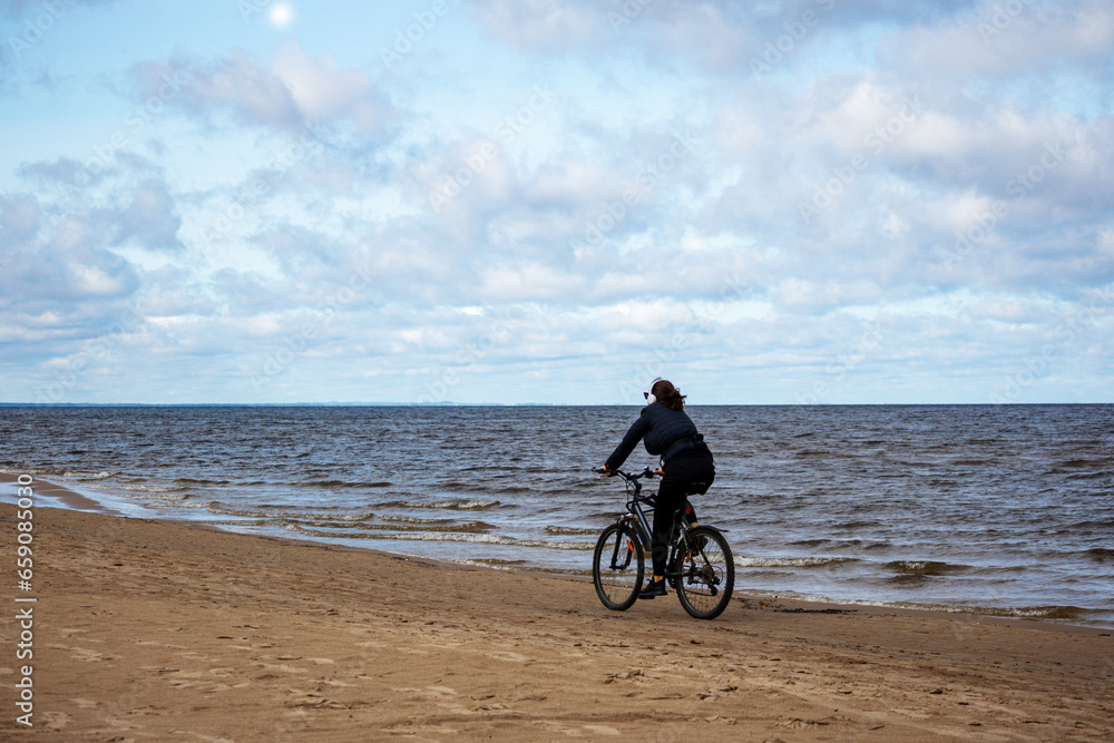 Fototapeta premium Along the seashore along smil'tim rides a cyclist with music headphones on his head