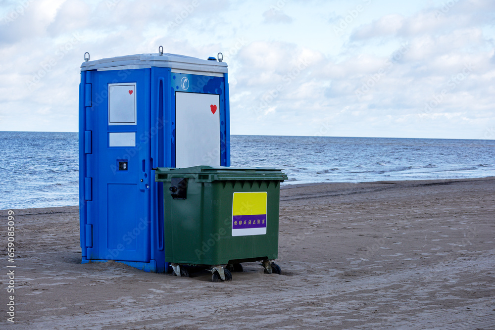 A dumpster and a blue WC stand on the sand in the seashore