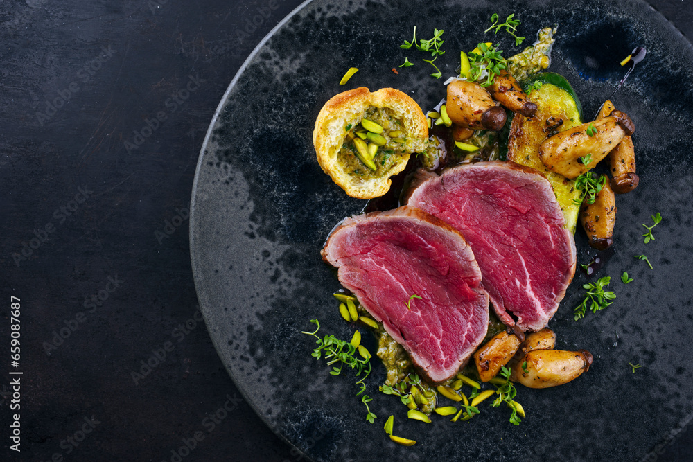 Fried Italian chianina beef fillet steak very rare with mushrooms, chopped pistachios and Beignet served as top view in a Nordic design plate with copy space left