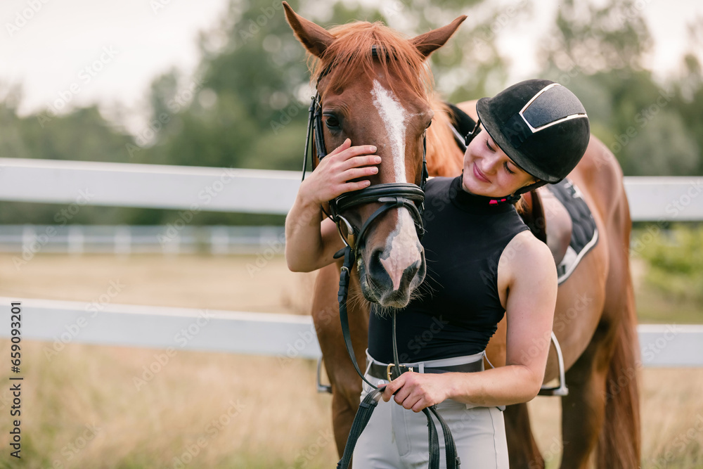 Obraz premium Woman with a black helmet stroking a beautiful chestnut horse head, close up shot. Human and animal relation concept.