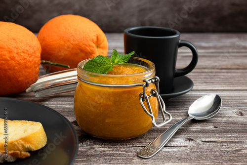 Delicious homemade orange marmalade in a glass jar. Healthy breakfast with homemade orange marmalade. Milk, coffee and jam on a slice of bread on a plate. Black.